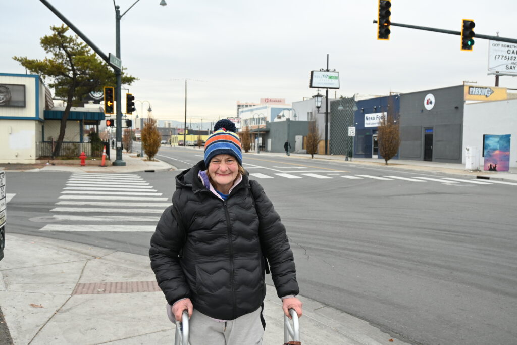 A portrait of a woman on a street corner in winter clothing holding a walker.