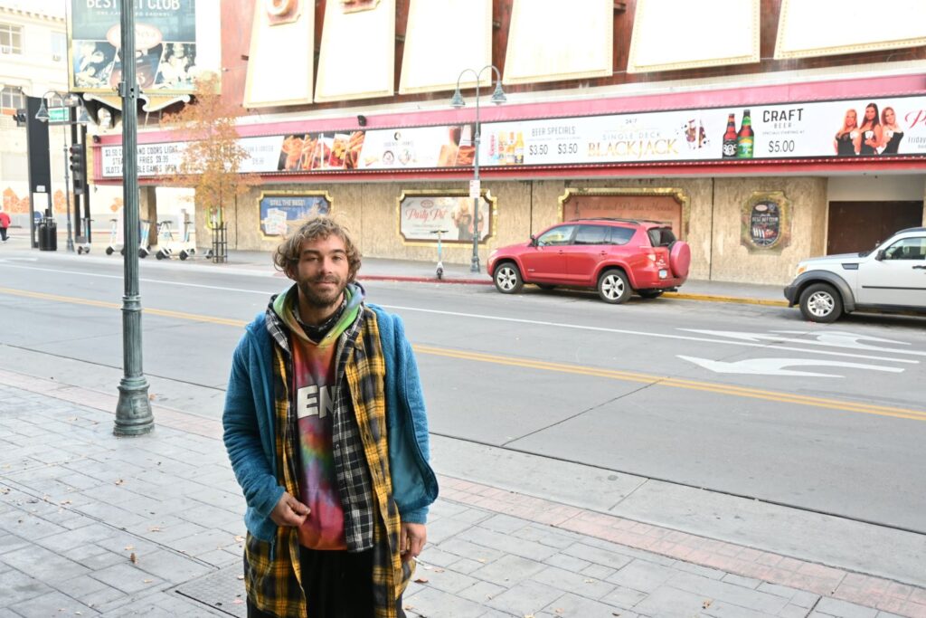 A young man is pictured bundled in winter clothing on a street. In one hand he holds a lit cigarette. 