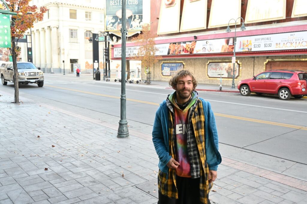 A man stands in the street looking into the distance, cigarette in hand.