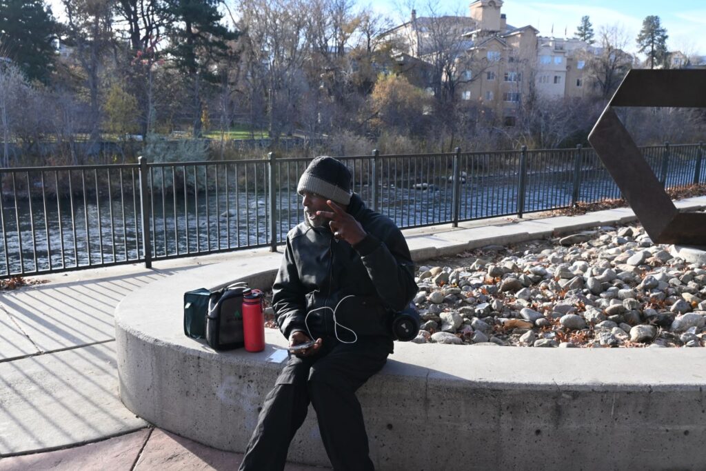 A man sitting by the river holds up the peace sign. 